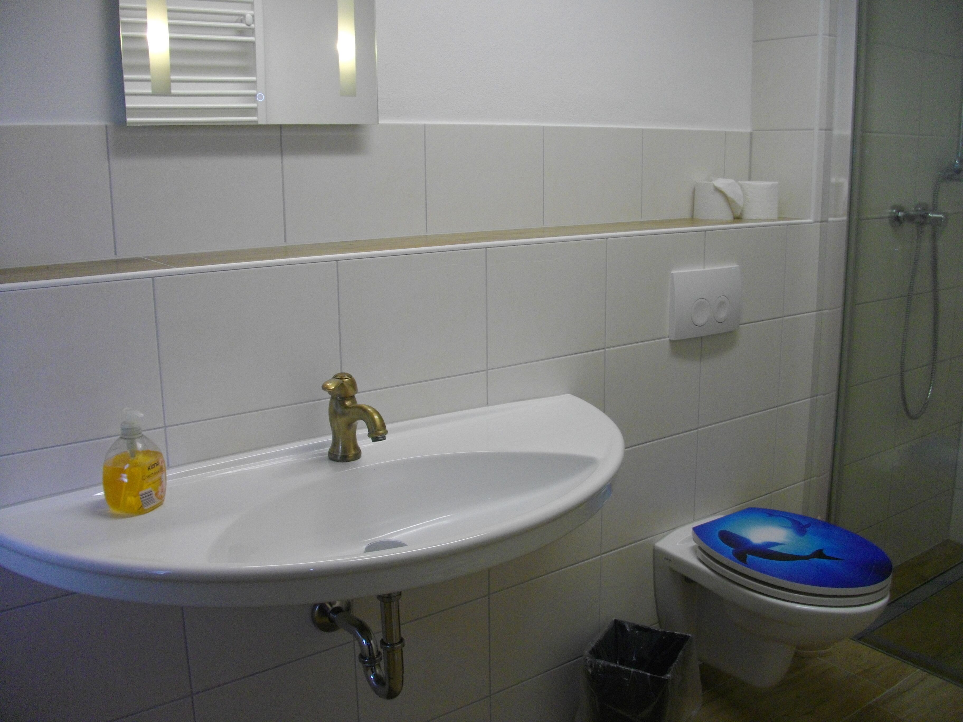 A bathroom with a white sink, a gold faucet, a toilet with a blue seat, and a glass shower enclosure.