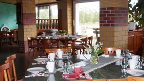 A dining area with a brick wall, wooden chairs, a marble table, and a view of the outdoors. - VierJahreszeiten Appartments (Lübben (Spreewald))