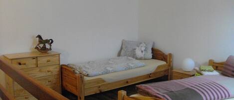 A small, simple bedroom with a single bed, a wooden dresser, and a rocking horse.