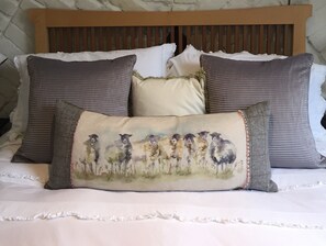 A bed with a wooden headboard, white bedding, and three pillows with a sheep design.