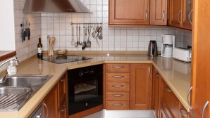 Een keuken met houten kastjes, een roestvrijstalen spoelbak, een inbouwoven en een gele hanglamp.