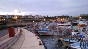 A marina with boats docked along a concrete quay, surrounded by residential buildings and a hillside. -   Sea  and Sun rise views. Villa with private pool and gated children Play Area. (paralimni)