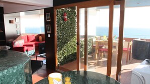 A room with a glass table, a red sofa, and a view of the ocean through a sliding door.
