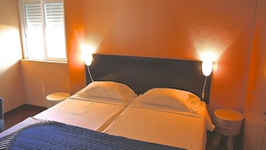A bed with a headboard, two bedside lamps, and a window with blinds.