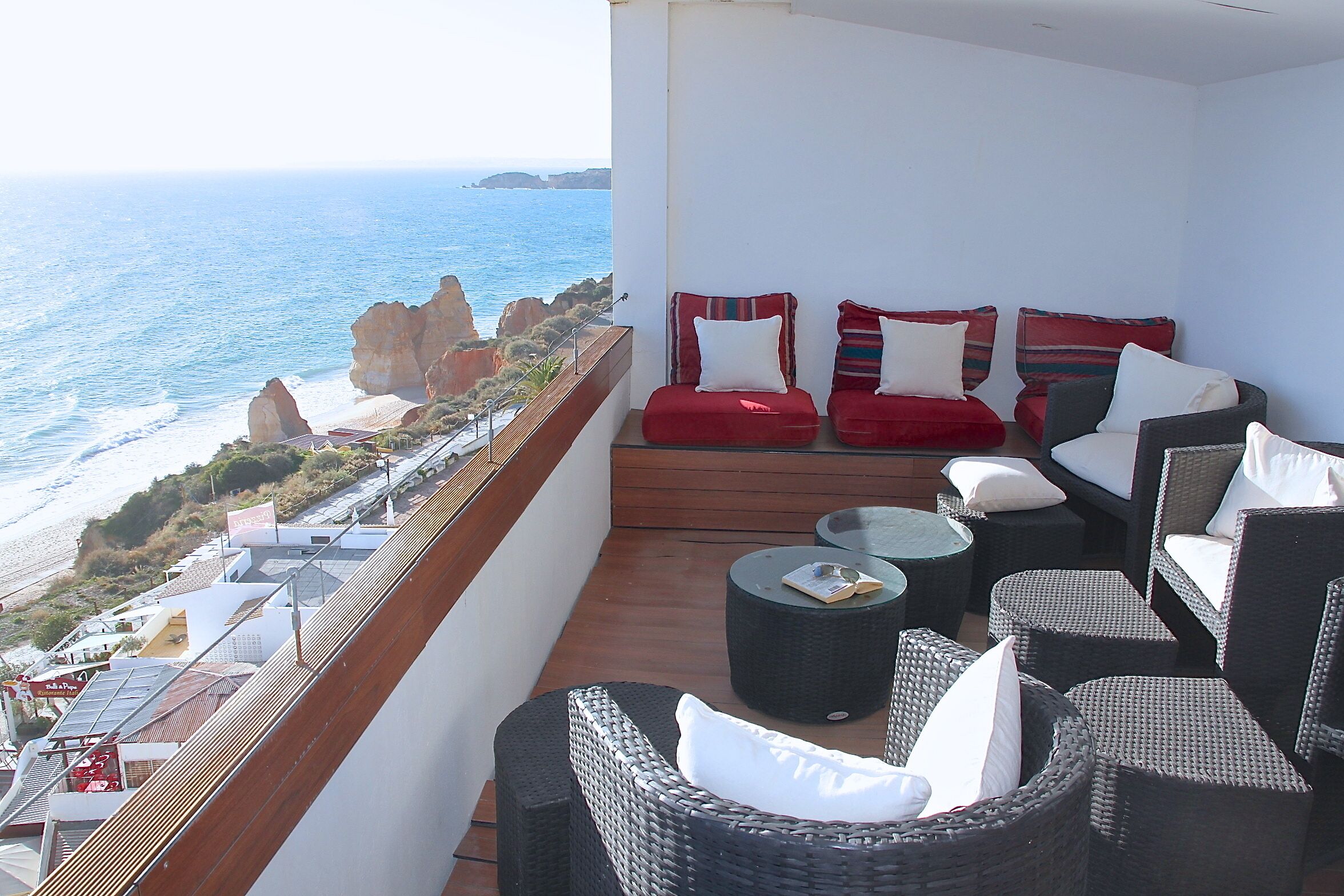 A balcony with wicker furniture, a view of the ocean, and rocky cliffs.