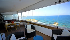 A deck with wicker furniture, a table, and chairs, overlooking a coastal view.