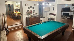 Een biljart in een ruimte met een houten plafond, een eethoek en een woonkamer met een open haard.
