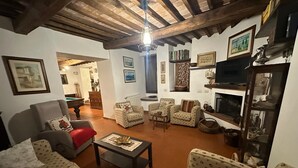 Een woonkamer met een open haard, meerdere fauteuils, een bank, een salontafel en een televisie.