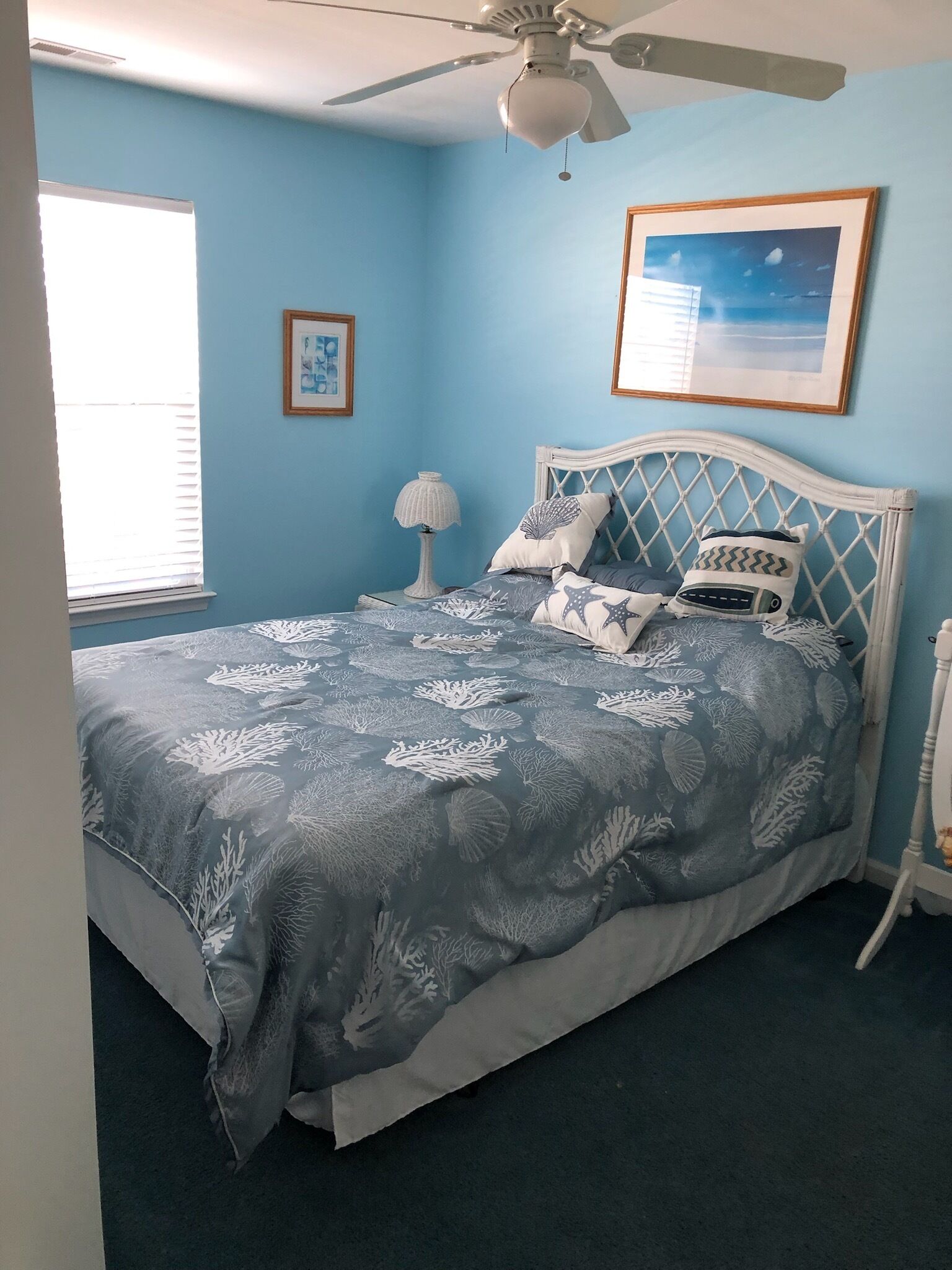 A bedroom with a bed, a ceiling fan, a nightstand, a lamp, and a framed picture on the wall.