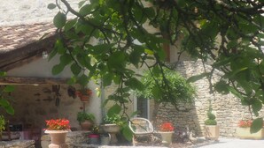 Un edificio rústico de piedra con techo de tejas, rodeado de macetas con plantas y un área verde.