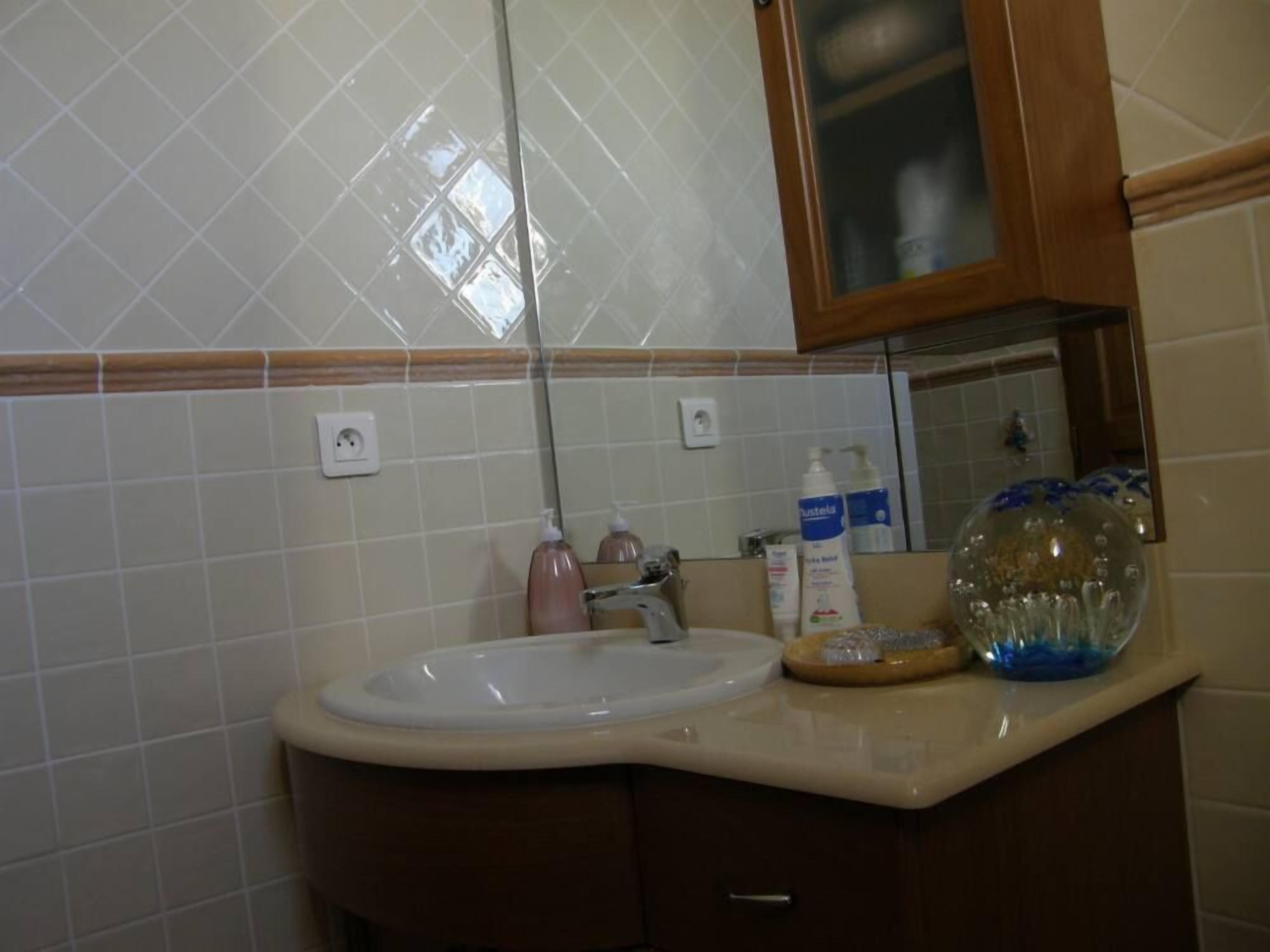 A bathroom with a white sink, a mirror, and a wooden cabinet. There are two bottles of hand soap and a glass soap dispenser on the counter.
