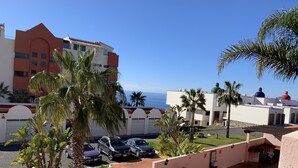 A hotel courtyard with palm trees, a swimming pool, and a view of the ocean.