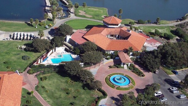An aerial view of a resort with a swimming pool, a tennis court, and a large building with a red roof.