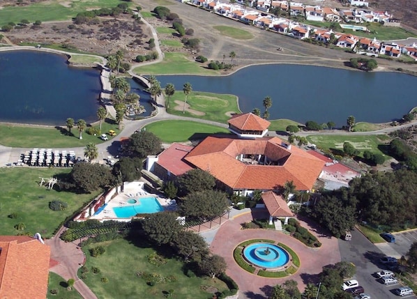 Ein Luftbild eines Resorts mit Schwimmbad, Tennisplatz und einem großen Gebäude mit rotem Dach.
