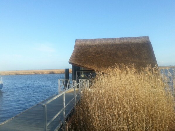 A wooden pier leading to a building with a thatched roof, surrounded by tall grasses.
