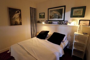 Una cama bien hecha con ropa de cama blanco y negro, una mesita de noche con una lámpara y una pared decorada con cuadros enmarcados.