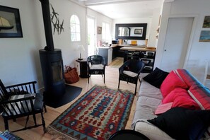 Una sala de estar con sofá, sillas, alfombra, chimenea y una cocina al fondo.