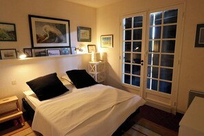A bedroom with a bed, a nightstand, a bedside table, a lamp, a window with curtains, and a door with glass panels. - Lovely country house close beach A0384 (Cap Ferret / Piraillan)