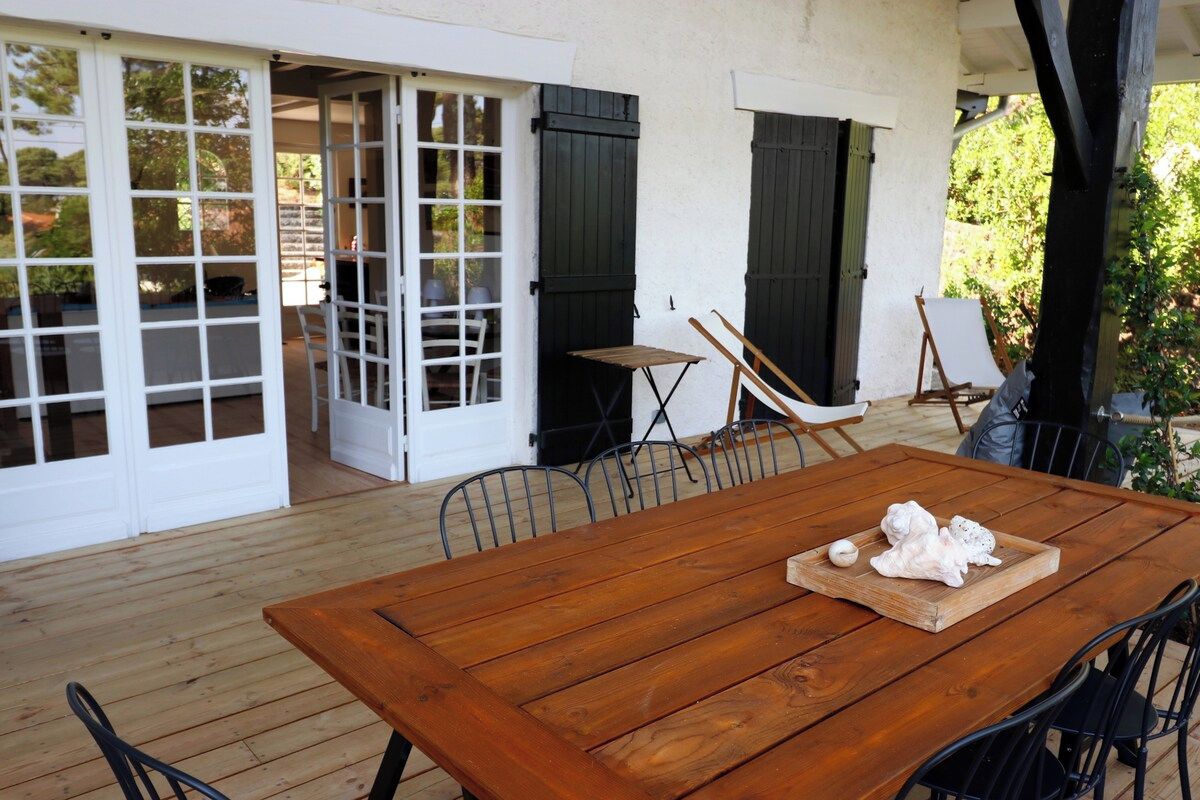 Une terrasse extérieure en bois, avec une table et des chaises, une chaise pliante et un petit chevalet.