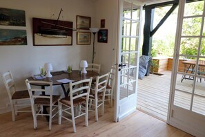 A dining area with a wooden table and white chairs, a set of framed pictures on the wall, and a view of the outdoor deck through a glass door. - Lovely country house close beach A0384 (Cap Ferret / Piraillan)
