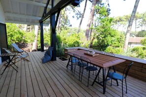 An outdoor wooden deck with a table and chairs, surrounded by trees and greenery. - Lovely country house close beach A0384 (Cap Ferret / Piraillan)