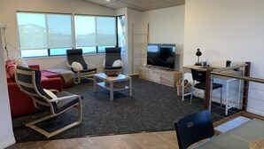 Una sala de estar moderna con un sofá, dos sillones, una mesa de centro, un televisor y un escritorio con una computadora.
