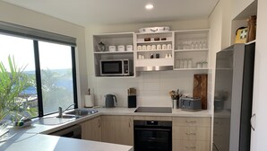 Una cocina moderna con microondas integrado, horno y refrigerador. Cuenta con un ventanal grande, gabinetes de madera y una encimera con diversos utensilios de cocina.