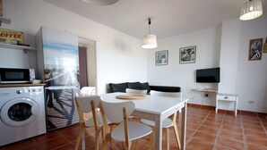 Un espace de vie compact comprenant un lave-linge, une table à manger avec des chaises, un téléviseur et des œuvres d’art accrochées aux murs.