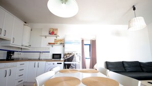 Une cuisine moderne avec des meubles blancs, une table à manger avec des sets de table, un canapé noir et une lampe suspendue.