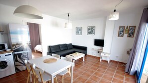 Un salon moderne avec un canapé, une table à manger et des chaises. La pièce est équipée d’un téléviseur, d’un lave-linge et d’un ventilateur.