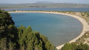 Eine Küstenlandschaft mit Sandstrand, klarem blauen Wasser und einer Hügelkette im Hintergrund.