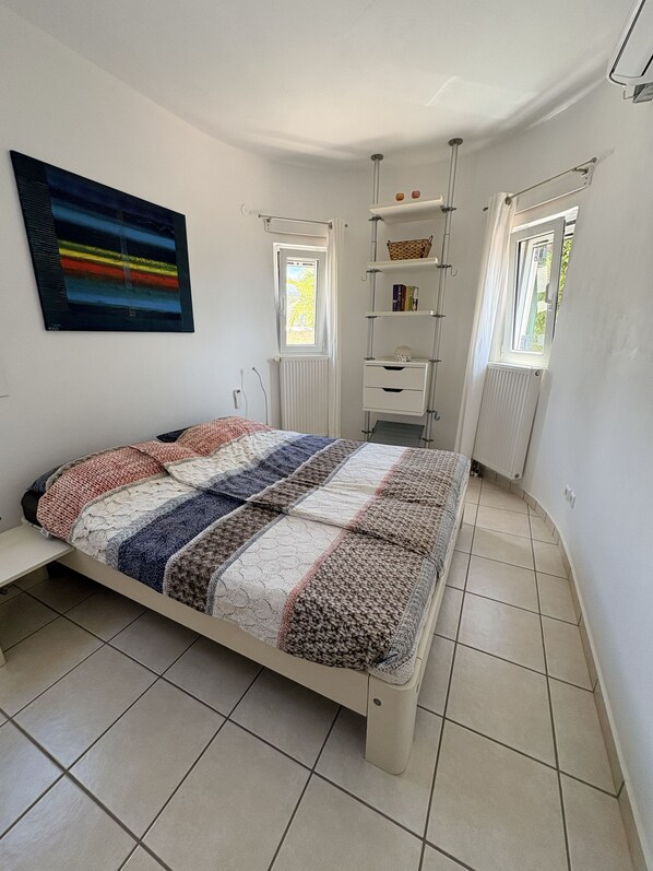 A bedroom with a bed, a radiator, a window, and a shelf with books.