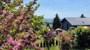 A garden with blooming pink flowers, a wooden structure, and a view of the countryside. - Adventure and Relaxation for you and your family in the Southern Bavarian Forest (Windorf)