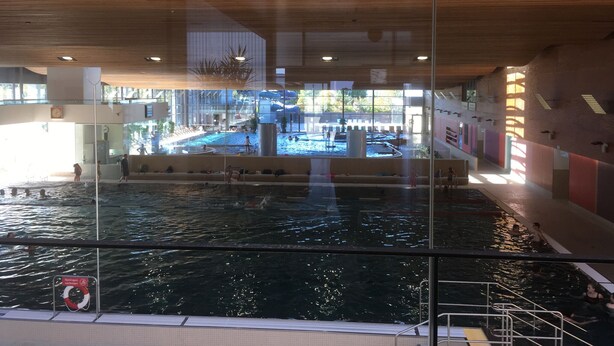 An indoor swimming pool with multiple lanes, a lifeguard stand, and a glass barrier. - Adventure and Relaxation for you and your family in the Southern Bavarian Forest (Windorf)