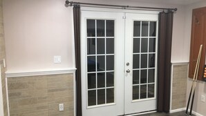 Une porte à deux battants avec des panneaux de verre, un rideau foncé, un cadre de porte en bois et une poignée de porte.