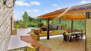 An outdoor patio with a wooden pergola, stone walls, and a pool in the background. - 4 bedroom, 2 bathroom converted Mill house with private pool.  Outdoor kitchen! (Poggio Camporgiano)