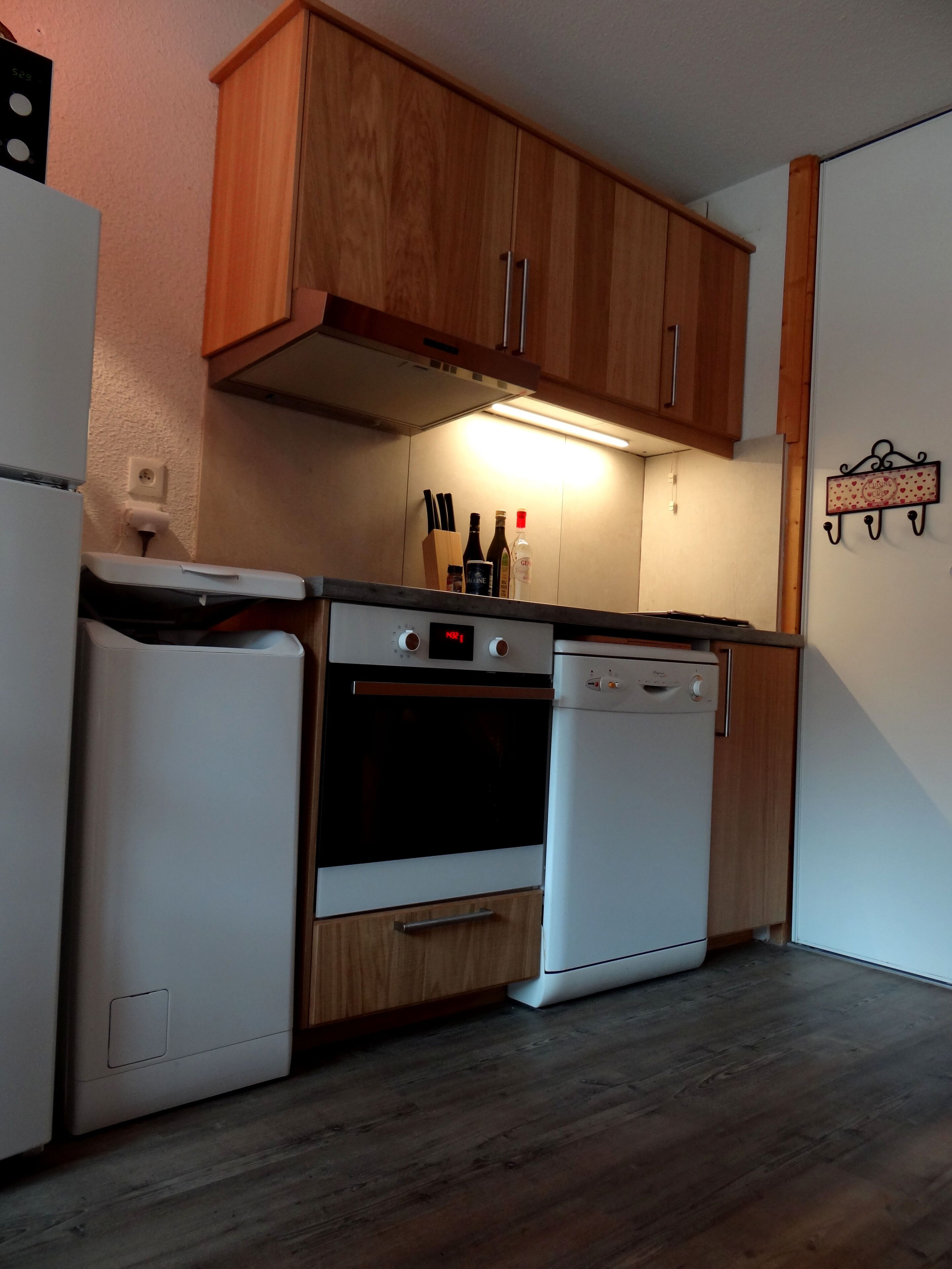 A compact kitchen with wooden cabinets, a built-in oven, a dishwasher, and a countertop with kitchen utensils.