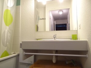 Een badkamer met een wit wastafelmeubel, spiegel en een groene beker op het aanrecht.