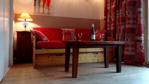 Ein gemütliches Wohnzimmer mit einer Holzsofa, einem Tisch mit Flasche und Gläsern, einer Lampe und einem Bild an der Wand.