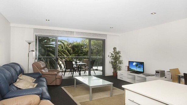 Un soggiorno moderno con divano, tavolino, televisore e un balcone con mobili da esterno.