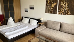 A bedroom with a bed, a sofa, a glass coffee table, a nightstand, a lamp, and artwork on the wall. - Holiday apartment K112 for 2-4 persons near the beach (Schönberg OT Holm)