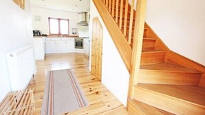 Une cuisine avec des meubles blancs, un escalier en bois et une fenêtre.