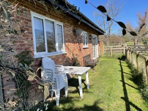 Une maison en briques avec un patio, une table blanche et deux chaises en plastique blanches.
