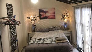 A bedroom with a bed, two bedside tables, a ceiling fan, a wall-mounted light fixture, a decorative wall piece, and a window with curtains. - TRADITIONAL SPANISH TOWN HOUSE INLAND SAX ALICANTE. SLEEPS 6 BED WIFI (sax)