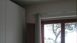 Une chambre à coucher avec un lit, une fenêtre avec des rideaux et une vue sur les arbres et les bâtiments à l’extérieur.