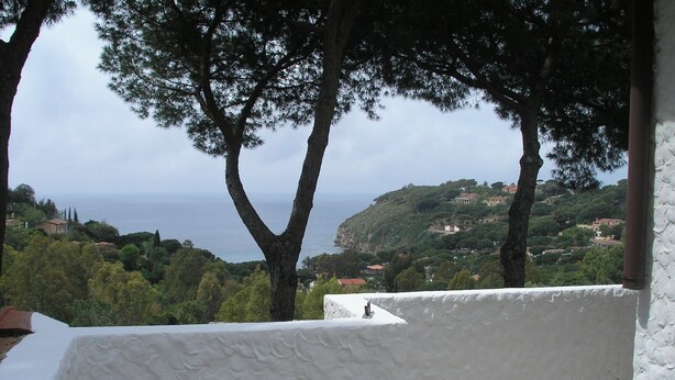Une terrasse offrant une vue sur la mer et les collines, des murs blancs et un sol carrelé.