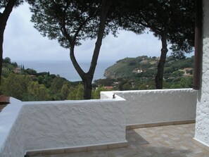 A terrace with a view of the sea and hills, white walls, and tiled flooring.