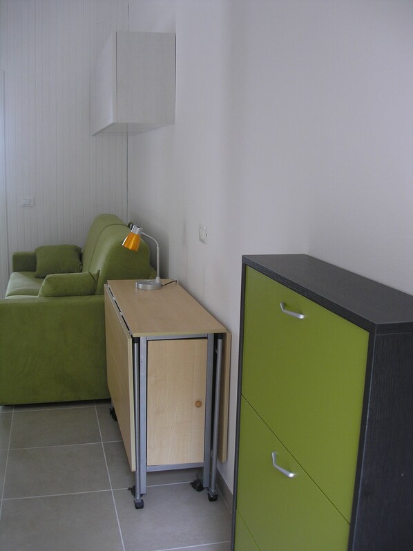 A small, neatly arranged room with a green sofa, a wooden desk with a lamp, and a green cabinet.
