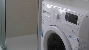 Un lave-linge dans une salle de bain dont les murs sont recouverts de carrelage et qui est équipée d’une porte de douche.