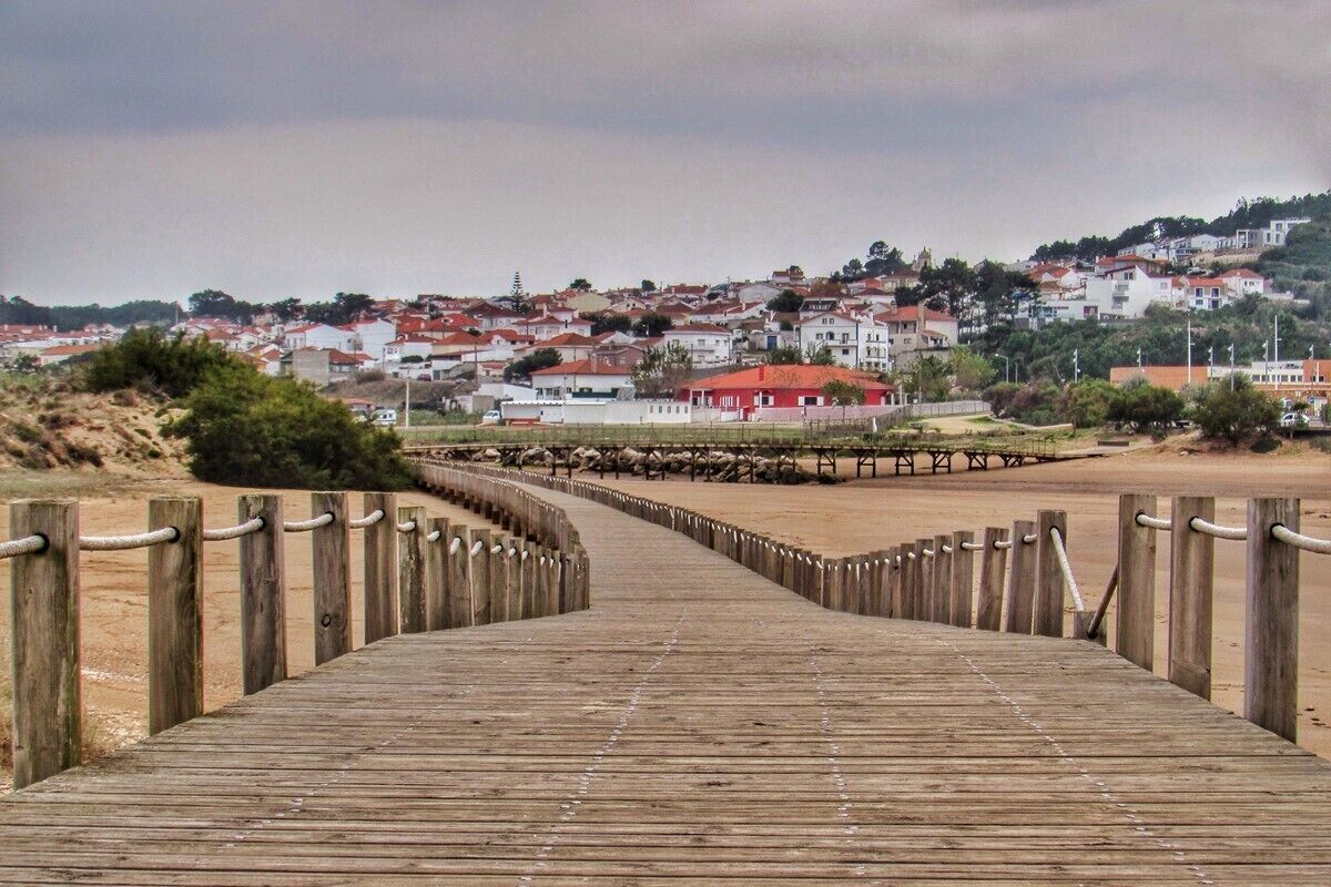A wooden boardwalk leading to a beach with houses in the background.